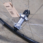Close-up of a bicycle hub with a cardboard piece attached, on a concrete surface.
