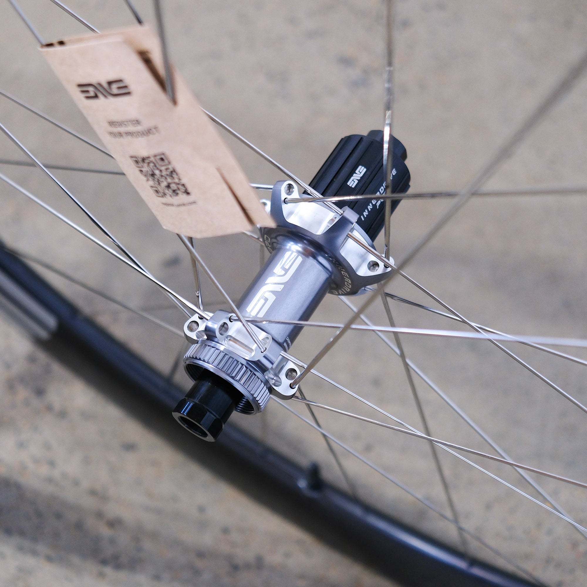Close-up of a bicycle hub with a cardboard piece attached, on a concrete surface.
